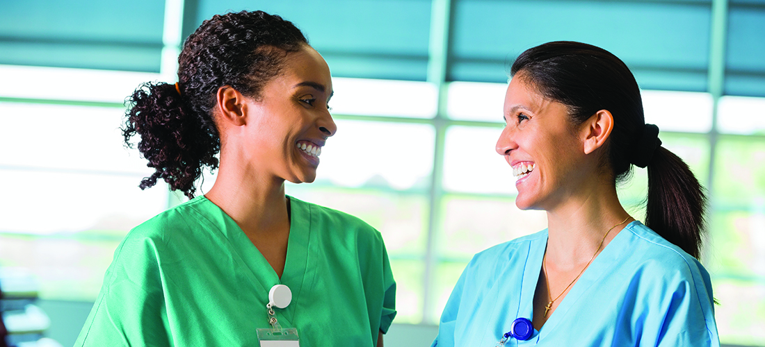 Two women in scrubs smiling at each other