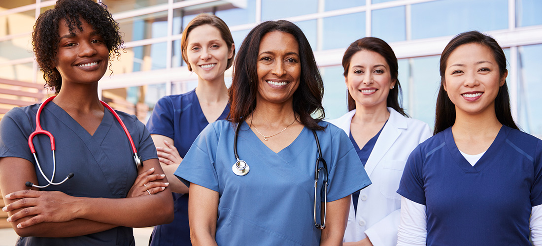 Group of smiling women dressed in various scrubs.