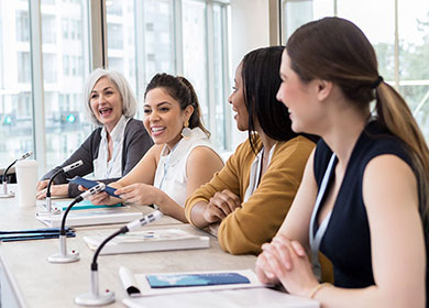 A group of four people sit at a table in front of microphones and smile.