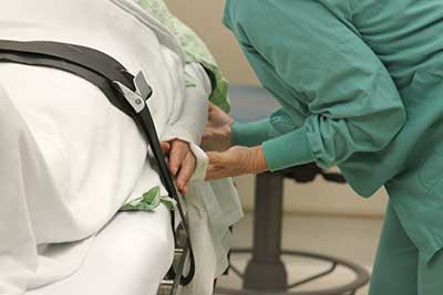 A surgical nurse in the OR tucks a patient's arm onto a operating room table