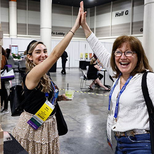 Two women giving a high five in expo hall.