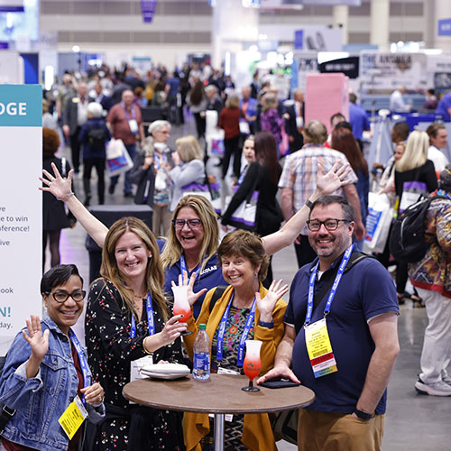 reception_500x500 Group of people posing with large crowd walking around Expo Hall in the background.