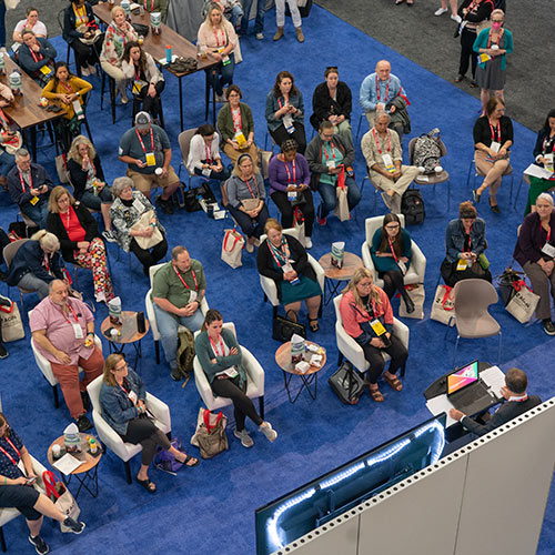 Crowd sits in Expo Hall listening to person on stage.